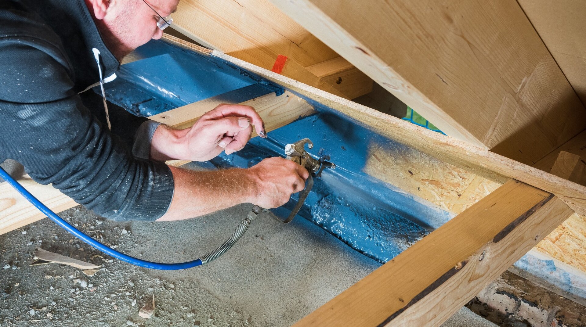 Baustelle Dachstuhl, Handwerker beim Sprühen von blauen Material auf die Dachbalken
