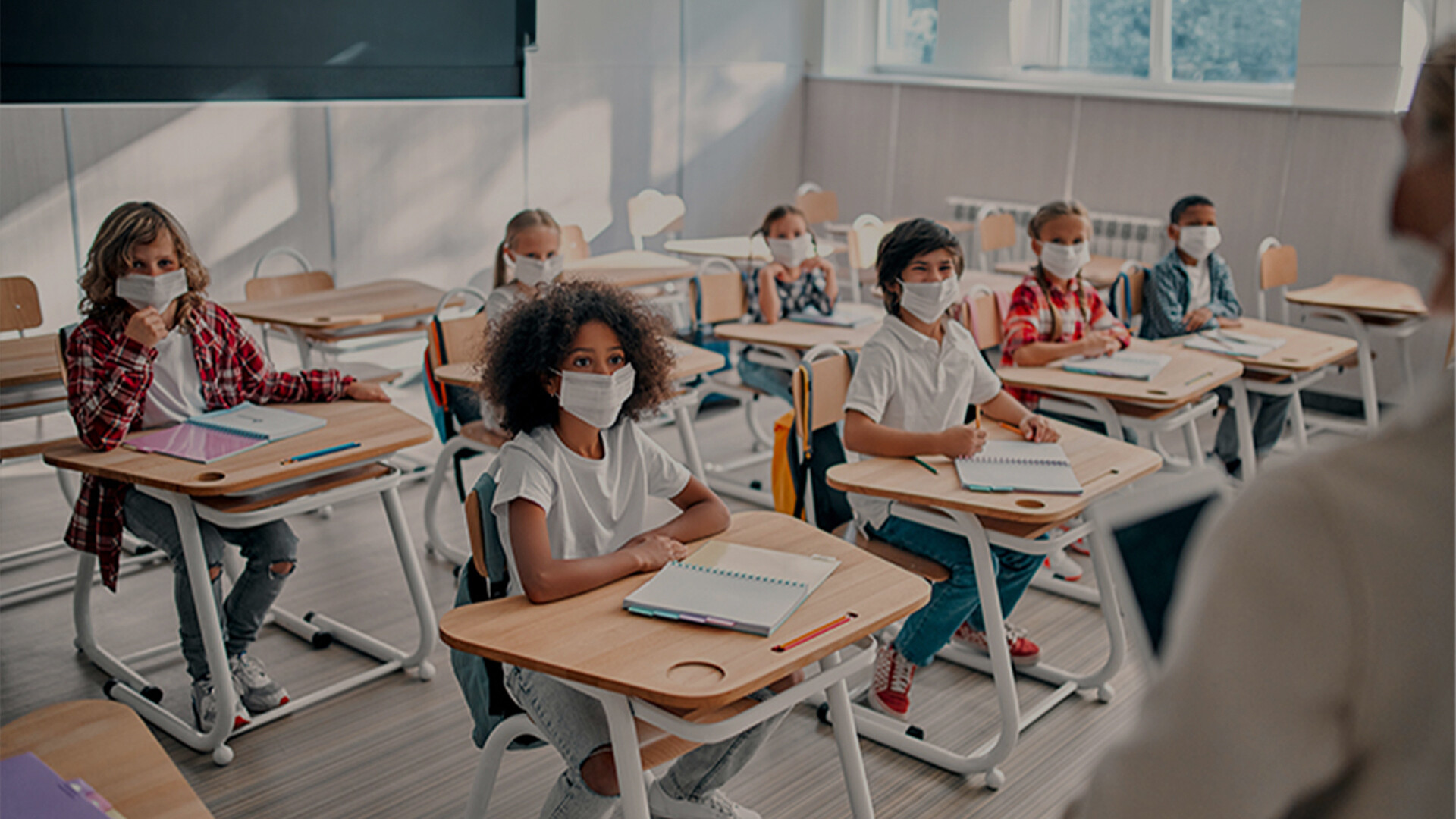 Mehrere junge Kinder sitzen in der Schule, alle haben Mundschutz auf.
